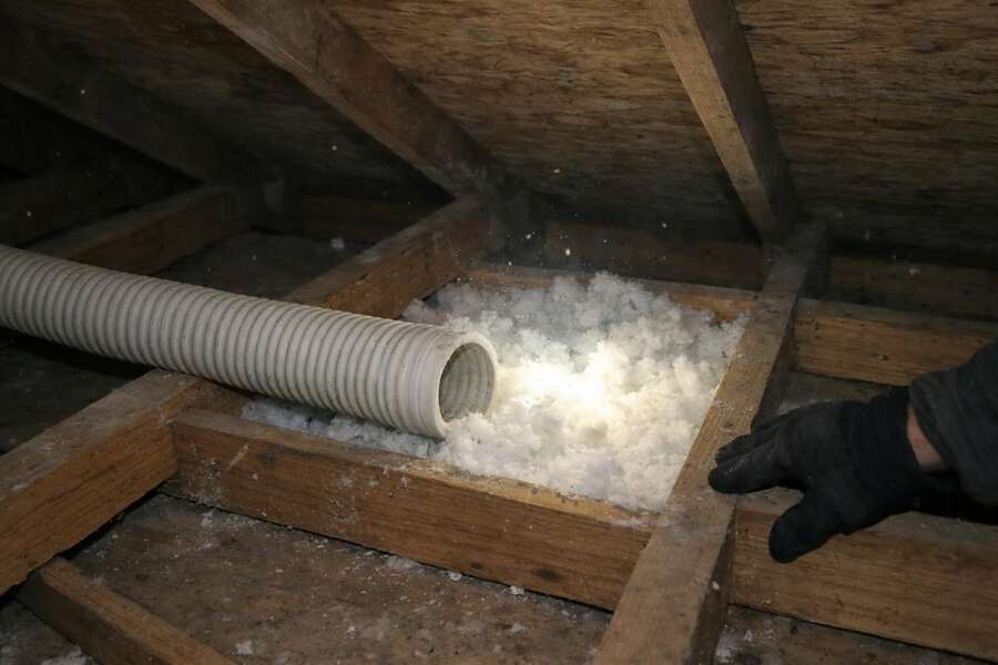 A blown-in insulation hose filling a joist bay with fresh loose-fill insulation