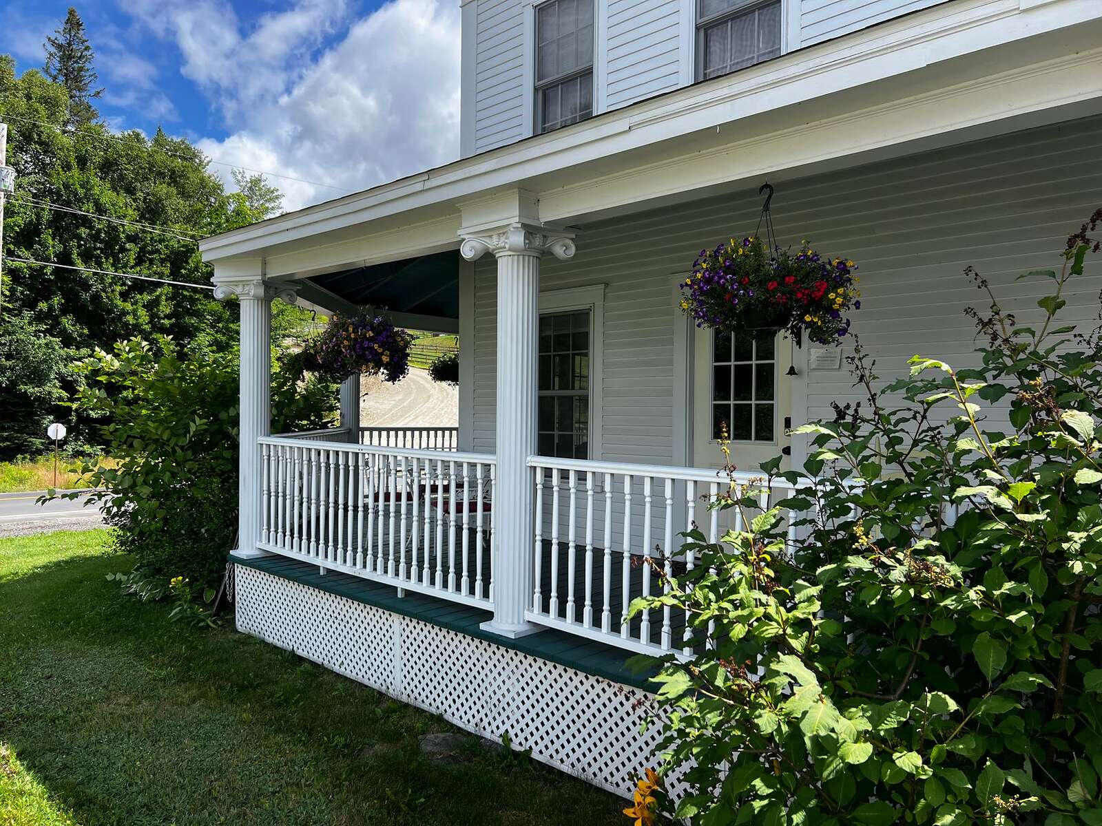 The front porch of a wood-frame bungalow with a swing and painted rail