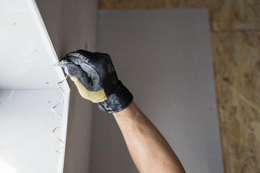 A gloved hand working at a drywall wall indoors