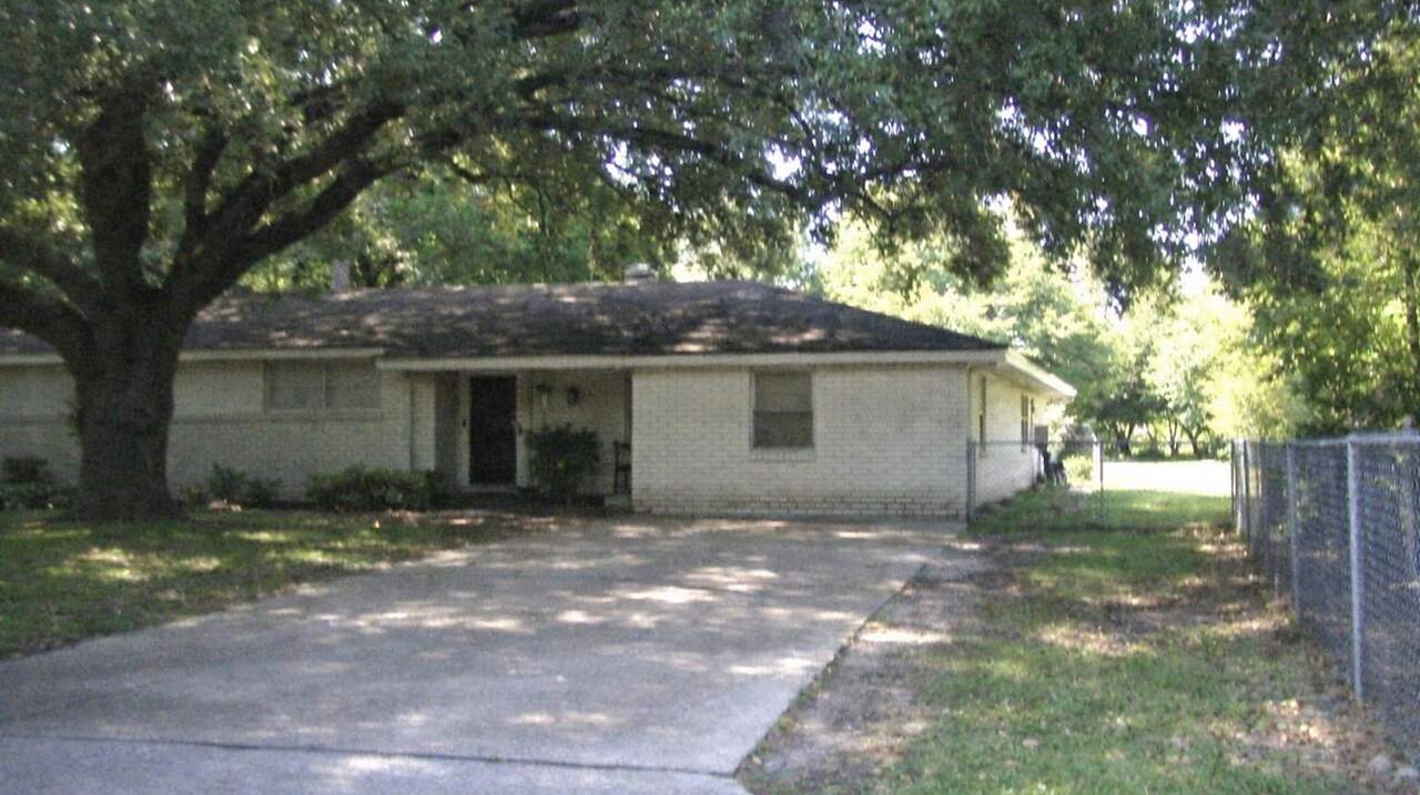 A single-story ranch house beneath spreading oaks