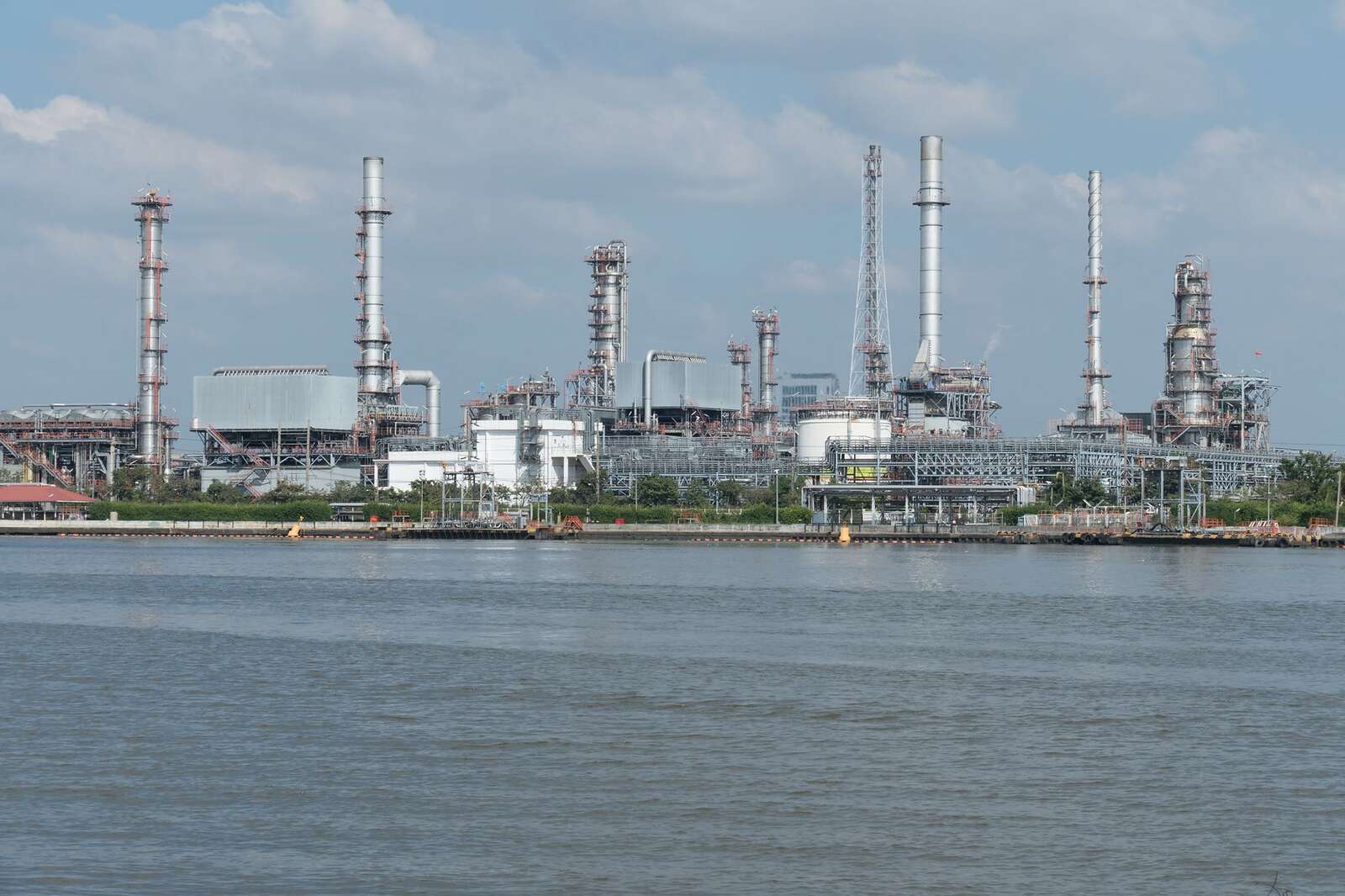 Refinery stacks and tanks along the water under a cloudy sky