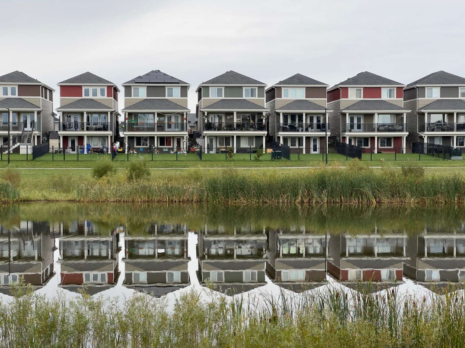 A row of houses reflected in a calm pond at the edge of a subdivision